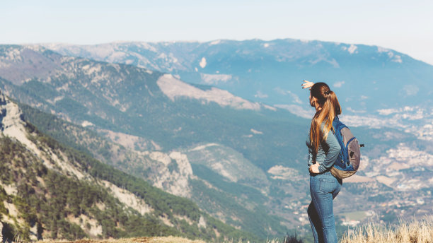 年轻美丽的姑娘独自在山间旅行，在春天或秋天，眺望远方，欣赏自然，岩石和绿色的森林，观赏风景。背包和运动装的背后，自由和轻盈。素材图片