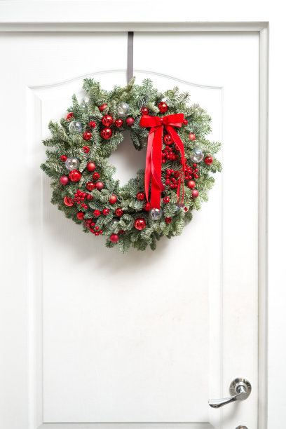 白色的门上挂着漂亮的新鲜云杉制成的红色圣诞花环。房子的入口。圣诞节的心情。圣诞树。图片下载