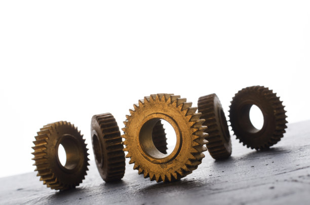 闪亮的齿轮在黑暗的表面上对抗明亮的背景。金属零件的特写图片下载