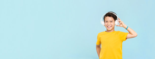 快乐微笑的混血男孩戴着无线耳机听音乐孤立在浅蓝色横幅背景与拷贝空间图片下载