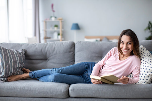 一个女人躺在公寓客厅的沙发上看书。图片下载