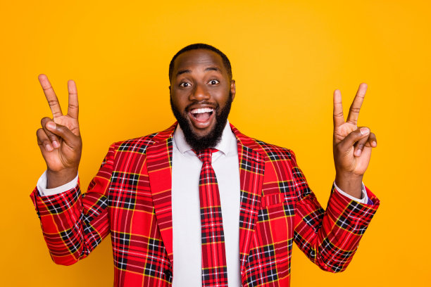 有吸引力的照片funky深色皮肤的家伙好心情举起手臂显示v符号符号穿格子红色服装外套衬衫领带孤立的黄色背景图片下载