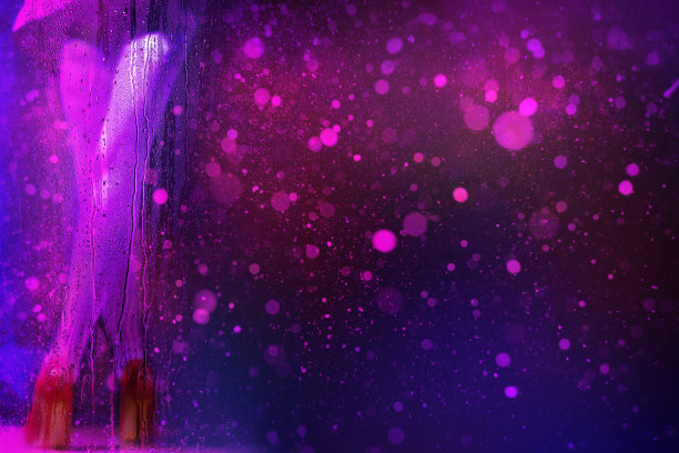 霓虹灯光下模糊的女性腿藏在带有雨滴的湿玻璃后面图片下载