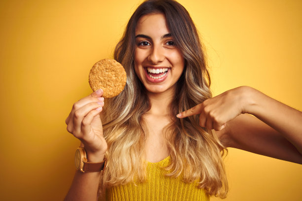 年轻漂亮的女人在灰色背景前吃饼干，惊讶地指着自己图片下载