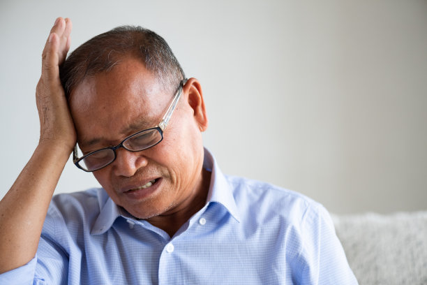 一个坐在沙发上头疼的亚洲老人。高级医疗保健的概念。图片下载