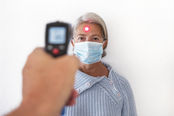 冠状病毒控制。为一位戴着医用防护口罩避免感染COVID-19冠状病毒的退休老人检查体温。疾病和检疫概念图片下载