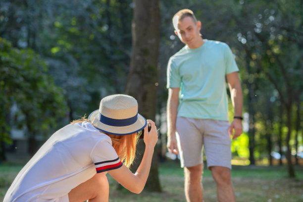 一对年轻的情侣在阳光明媚的夏日公园里拍下彼此的照片。图片下载
