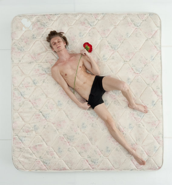 男性躺在卧室的白色背景前，穿着内衣，拿着玫瑰花图片下载
