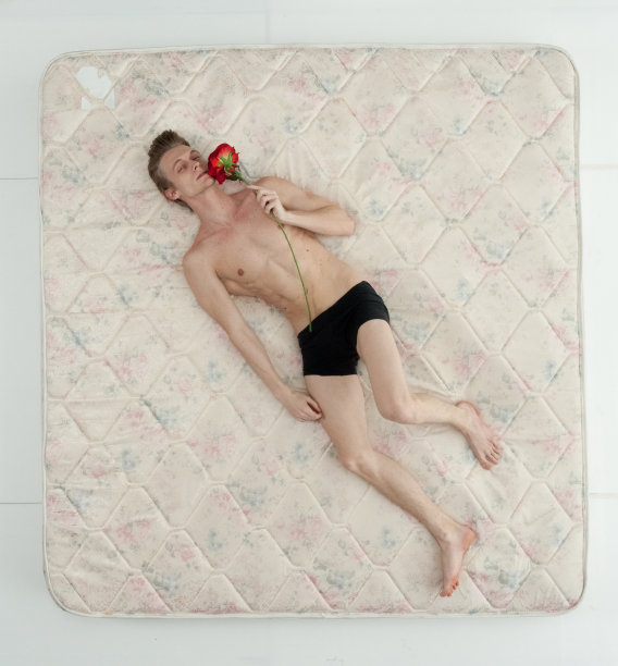 年轻男子在卧室的白色背景下醒来，穿着内衣，拿着玫瑰花图片下载