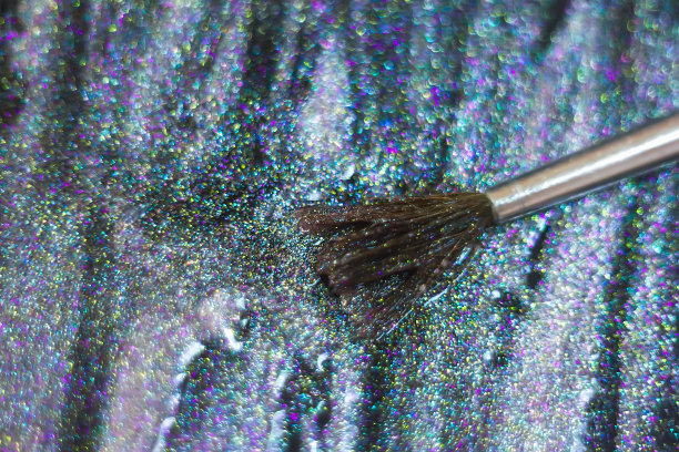 刷子和闪光粉的特写。非常浅的焦点在笔尖。指甲的质地闪闪发光。刷子旁边有一瓶指甲油。化妆品广告的概念图片下载