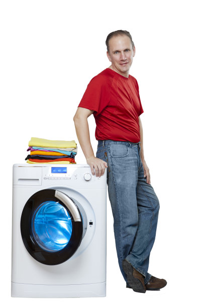 微笑的男人靠近洗衣机和一堆明亮的亚麻，孤立在白色的背景图片下载