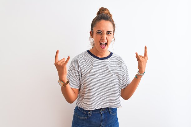 年轻的红发现代女性梳着发髻，在孤立的背景下大声呼喊，用疯狂的表情做着摇滚符号，举起双手。音乐明星。沉重的概念。图片下载