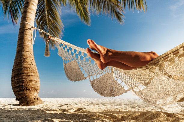 从沙滩上的吊床上看到的难以辨认的女人的腿。图片下载
