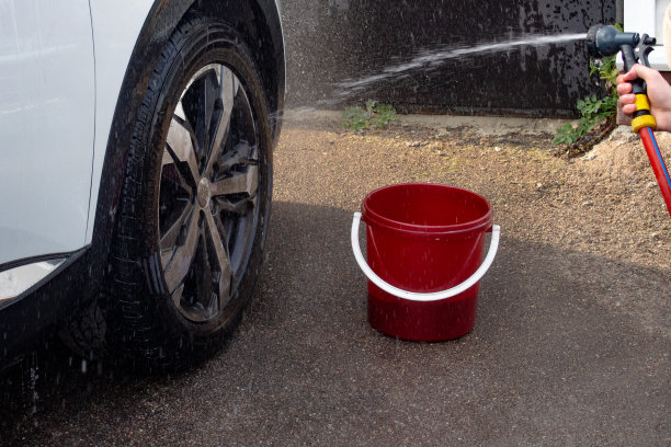 一个穿绿色夹克的人用水管冲洗一辆白色的汽车图片下载