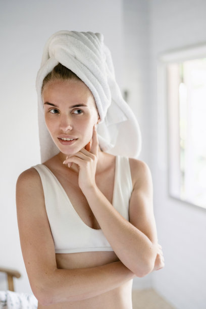 年轻的成年女性站在白色的浴室里，头上盖着毛巾图片下载