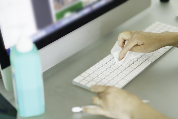 一名妇女正在为她的键盘表面消毒，以抵御冠状病毒-新冠肺炎全球爆发期间的病毒和细菌。图片下载