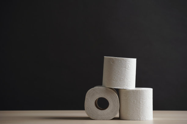 许多卫生纸卷堆成金字塔状。柔软的卫生纸。黑色背景上的木桌图片下载