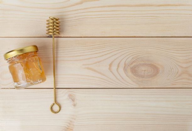 金属蜂蜜勺和蜂蜜罐。木头的背景。平的。图片下载