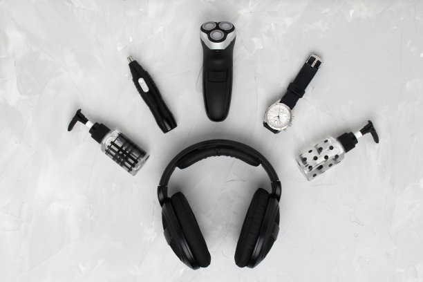 平躺电动剃须刀，鼻子和耳朵修剪器，须后水，手表和黑色耳机。男士的配饰呈半圆形。早上保健概念。黑白照片。图片下载