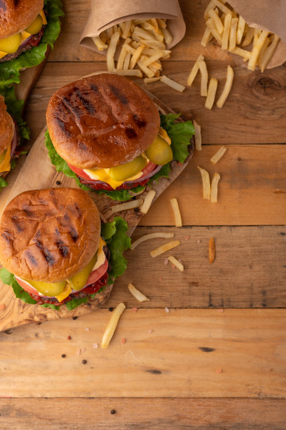 烤汉堡配牛肉，芝士，生菜，洋葱，番茄，黄瓜和酱汁。在切菜板上的木桌上放着自制的食物和炸薯条。美味的芝士汉堡。前视图。乡村风格的照片图片下载