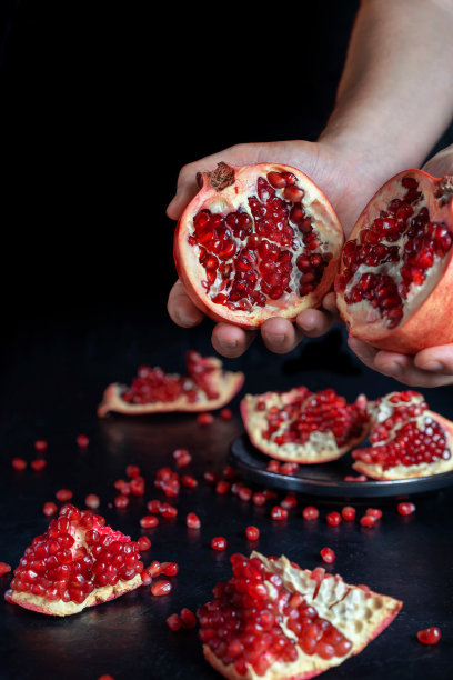 两半石榴在男性的手中。桌子上有一个石榴。图片下载