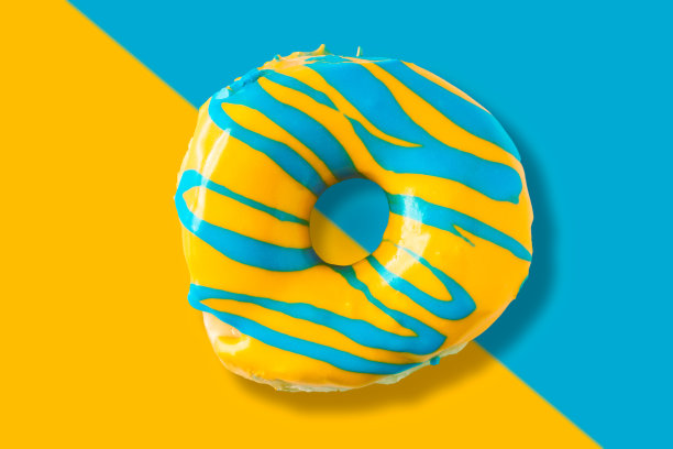 鲜艳明亮的黄色和蓝色釉面开胃甜甜圈在分裂的颜色背景。俯视图的美味看起来甜甜圈。图片下载