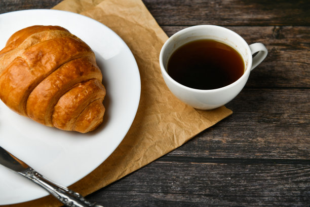 早餐,羊角面包。清晨的开始。新的法国羊角面包。木质背景上放着咖啡杯和新鲜烘焙的羊角面包。从以上观点。早餐有羊角面包和咖啡图片下载