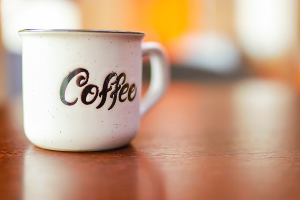 珐琅白色金属杯与铭文咖啡木桌上模糊的背景。图片下载