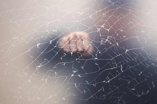 男性拳头后面的哑光玻璃墙与裂缝图片下载