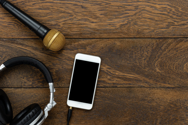 音乐和技术概念的表顶视图。白色智能手机与耳机和麦克风平铺在现代乡村木制的家庭办公桌子上。复制空间的创意设计。图片下载