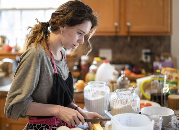 一个年轻女子在家里的厨房里烤香蕉面包，然后切黄油加入面糊。图片下载