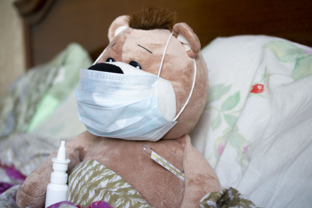 一只泰迪熊躺在床上，戴着医用口罩，还带着温度计。图片下载