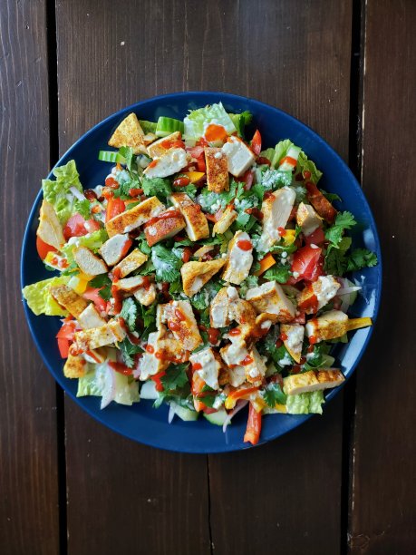 健康的鸡肉沙瓦玛沙拉，配有长叶莴苣，甜椒，香菜，西拉查酱，放在一个蓝色的盘子和一张木桌上图片下载