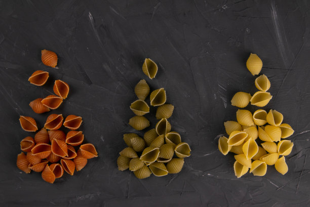 在黑板背景上的干贝壳意面俯视图。三个三角形的滑梯，上面铺着红色、绿色和黄色的贝壳意面图片下载