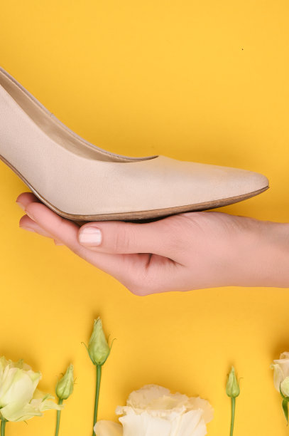 女鞋的概念。女人的米色鞋子上有花的手。背景是黄色的。米色鞋子，女孩的手。壁纸和鲜花。写的地方图片下载