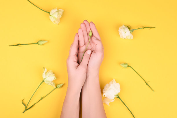 手靠近黄色背景上的花。皮肤护理。为题词的地方。平躺图片下载
