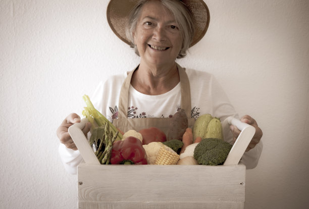 一个骄傲和快乐的老年妇女展示她的蔬菜花园的收获准备出售。健康饮食的丰富蔬菜品种。爱好养老金领取者的概念图片下载