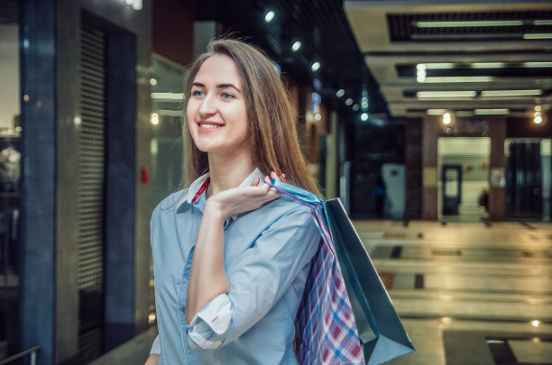 美丽的年轻棕色头发的长发女孩肩上背着许多包裹在购物中心。开朗、快乐的购物女郎图片下载