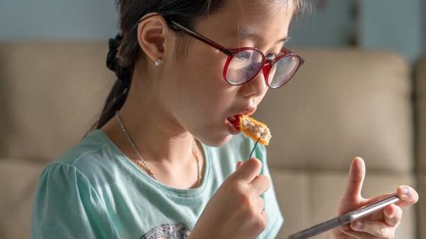 一个小女孩吃饭时看智能手机的照片图片下载