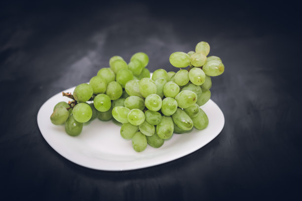 绿色多汁的新鲜葡萄放在一个白色的盘子上，在深黑灰色的艺术背景上图片下载