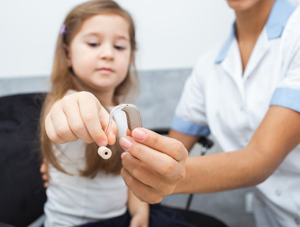 一个听力专家和一个小女孩的手拿着一个助听器。为孩子选择助听器。听到诊所图片下载