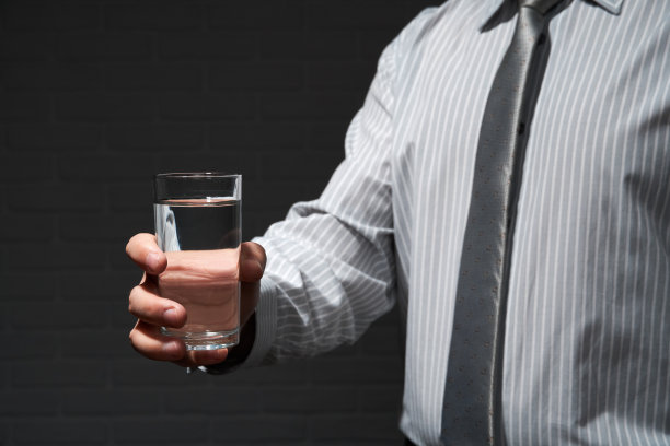 商人特写肖像，他站着摆姿势，用一杯水，深色的墙背景图片下载