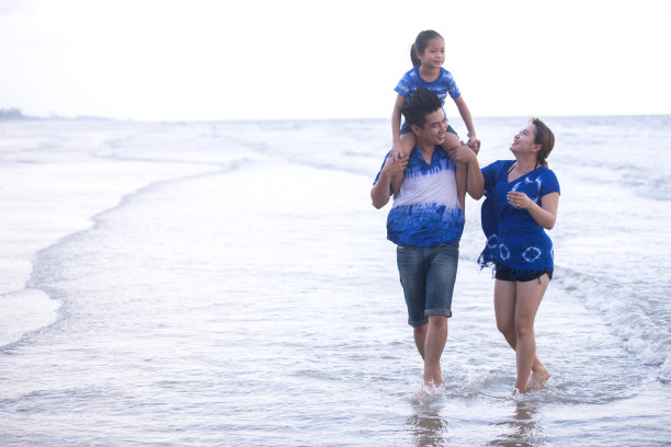 亚洲家庭穿着蓝色调的服装在海滩上玩得很开心。家庭良好关系概念图片下载