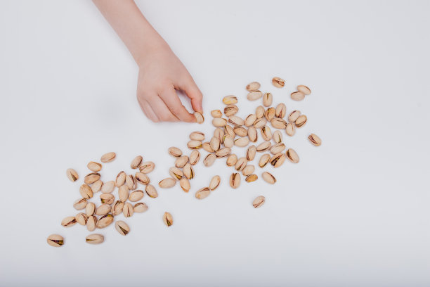 靠近，孩子的手与许多开心果孤立在白色的背景，图片下载