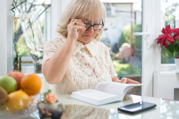 漂亮的老女人戴着眼镜在家里看书图片下载