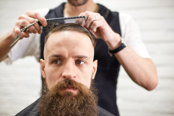 现代理发店里的野蛮人。理发师给留长胡子的男人做发型。美发师用理发器做发型图片下载