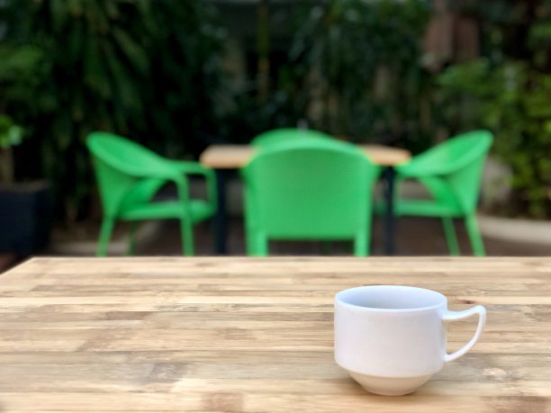 白色的咖啡杯放在桌上，模糊的绿色椅子背景图片下载