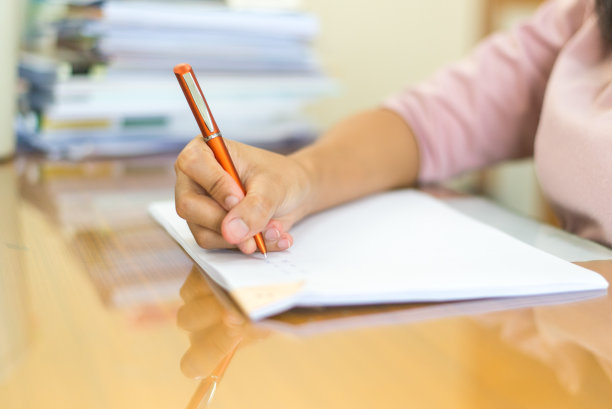 人们在家里的办公桌前写书。用手拿着纸上的橙色笔图片下载