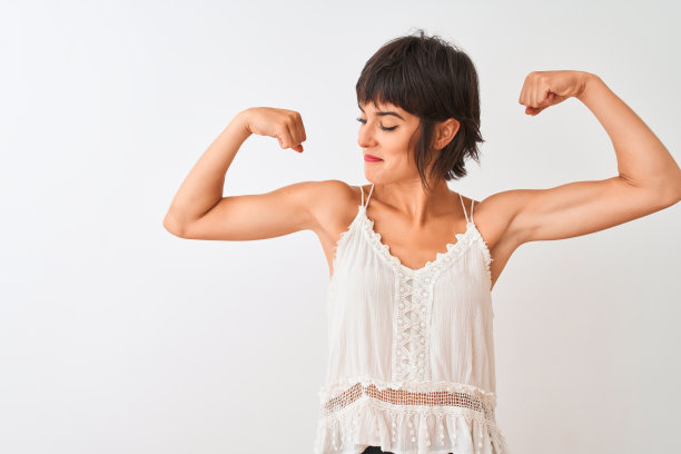年轻美丽的女子穿着夏季休闲t恤站在孤立的白色背景显示手臂肌肉自豪地微笑。健康的概念。图片下载