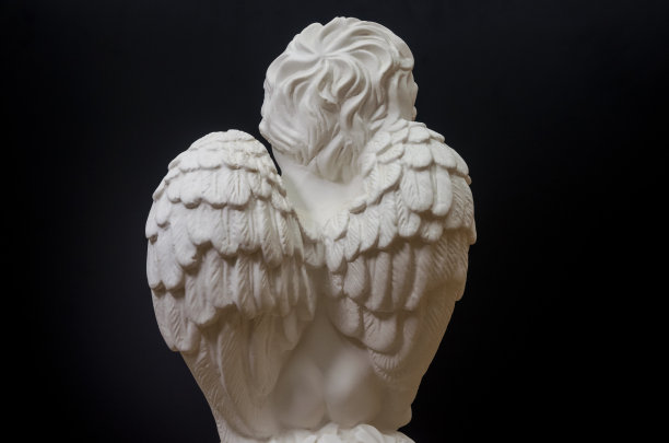 照片中的小雕像，以黑色背景为背景，背上有天使的翅膀。一个带着翅膀的天使的照片图片下载